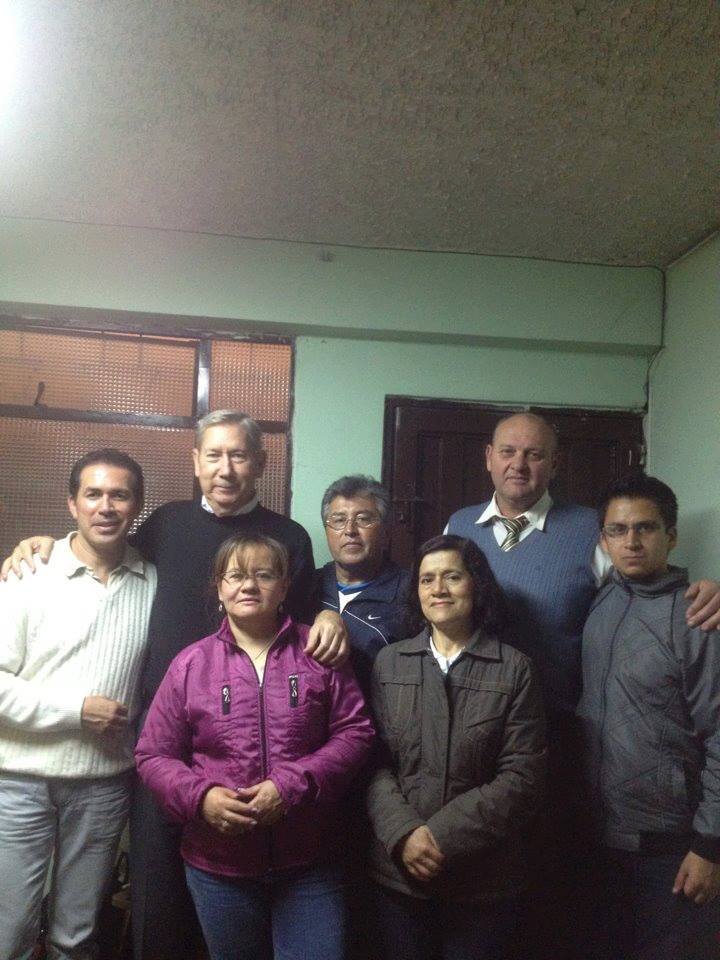 Group of seven people posing indoors, wearing casual jackets, with a neutral background.