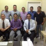 Group of men in an office setting, two seated, seven standing, dressed in business and casual attire.