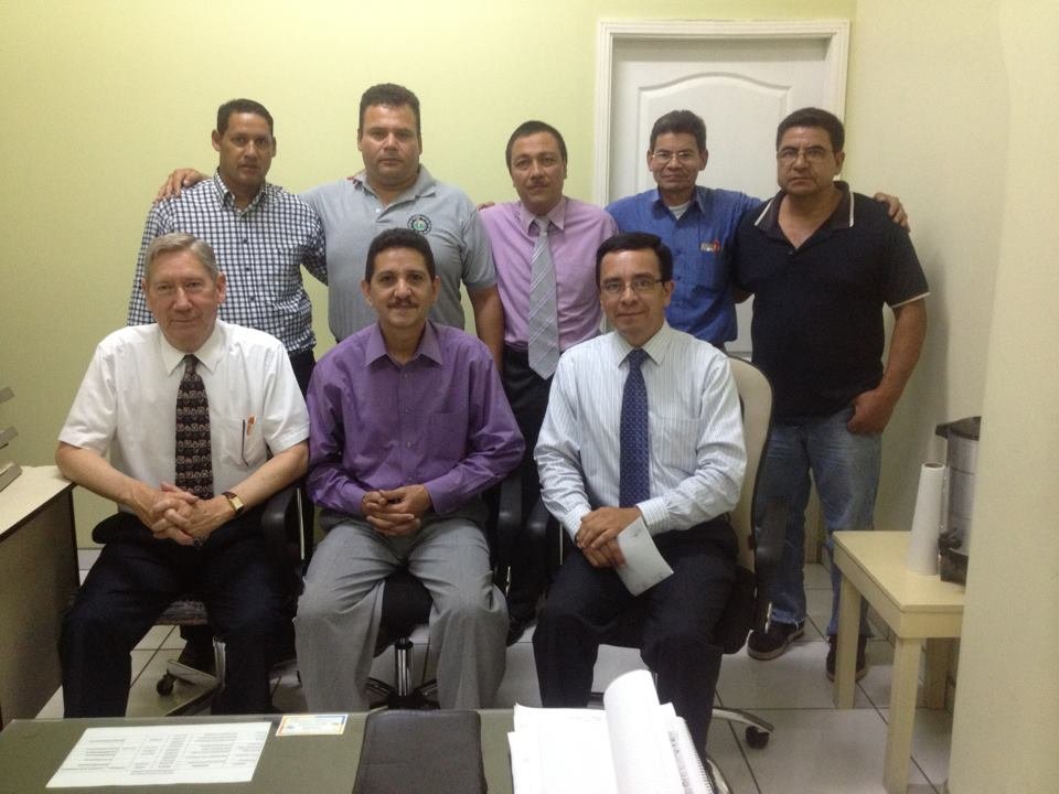 Group of men in an office setting, two seated, seven standing, dressed in business and casual attire.