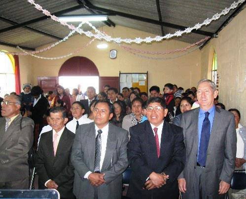 Group of people attending a formal event in a decorated room with men in suits standing in the front row.
