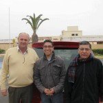 Three people smiling in front of a car at Coronel FAP Carlos Ciriani Santa Rosa Airport, Tacna, Peru.