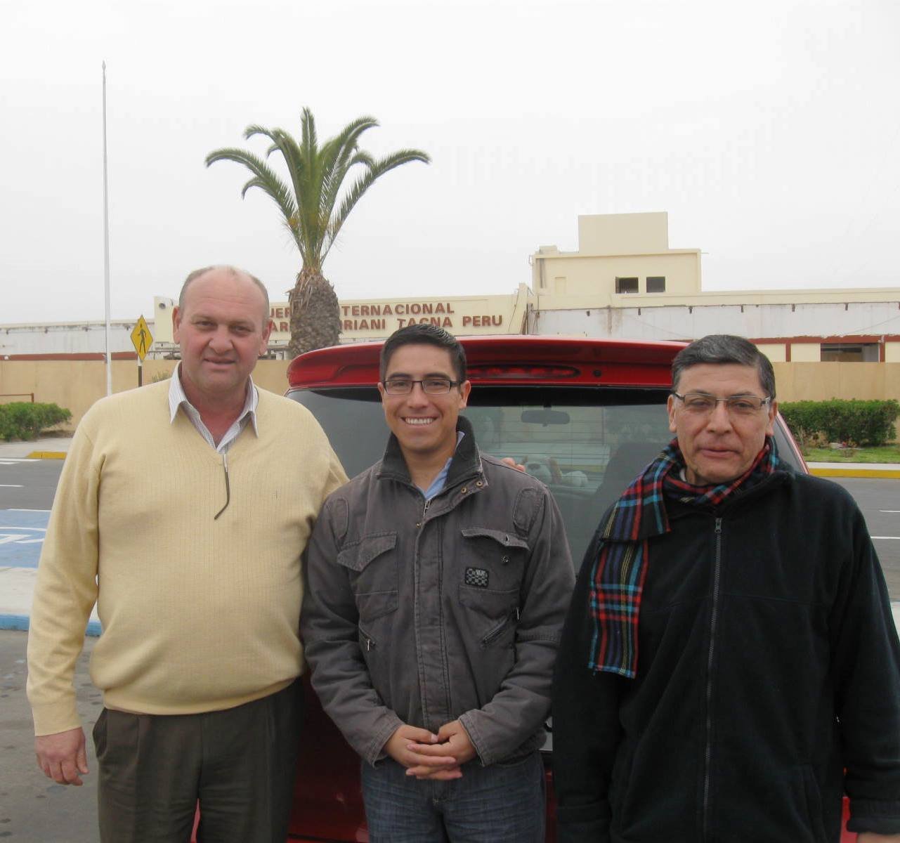 Three people smiling in front of a car at Coronel FAP Carlos Ciriani Santa Rosa Airport, Tacna, Peru.