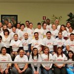 Group of people wearing matching shine shirts in a community gathering, seated and standing indoors.