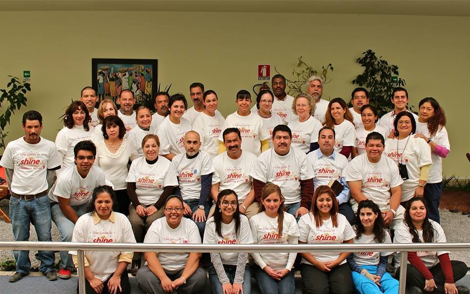 Group of people wearing matching shine shirts in a community gathering, seated and standing indoors.