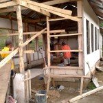 Construction workers building a wooden frame house with corrugated metal roof in progress.