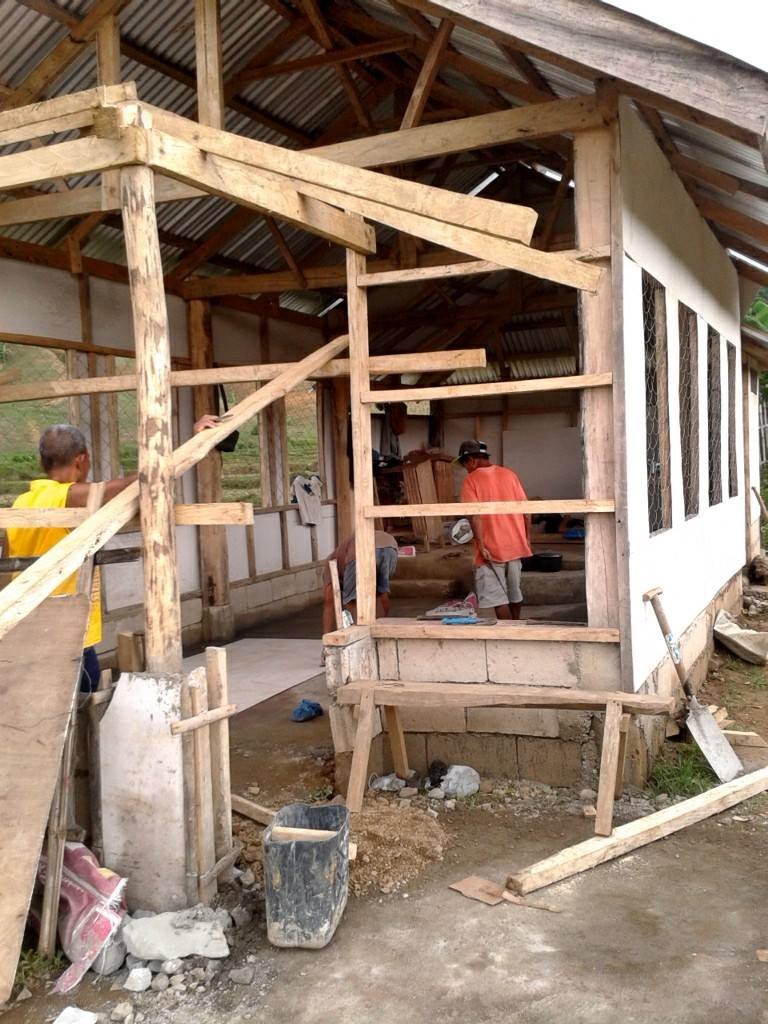 Construction workers building a wooden frame house with corrugated metal roof in progress.