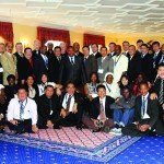 A diverse group of people at a conference event, posing indoors on a patterned carpet.