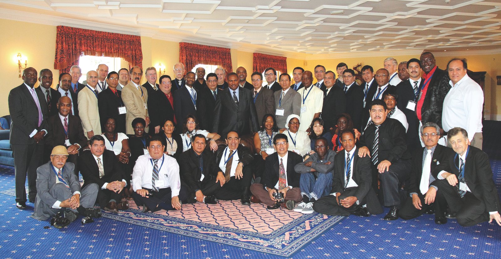 A diverse group of people at a conference event, posing indoors on a patterned carpet.