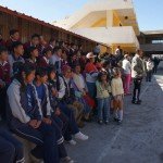 A group of students and adults gather in a school courtyard during a sunny day, with a focus on community and education.