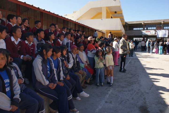 A group of students and adults gather in a school courtyard during a sunny day, with a focus on community and education.