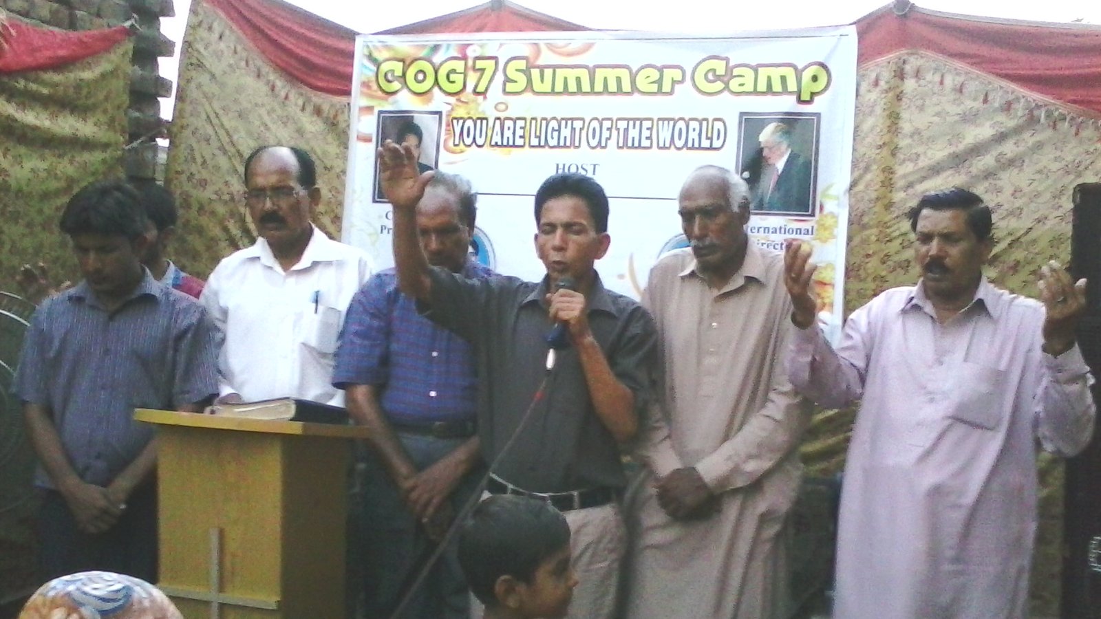 People praying at COG7 Summer Camp event, banner reads You Are Light of the World.