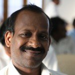 Smiling man in a white shirt at an indoor gathering, creating a warm and inviting atmosphere.