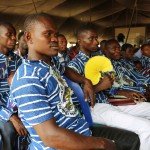 Group of men in blue and white striped clothing attending an event under a tent.