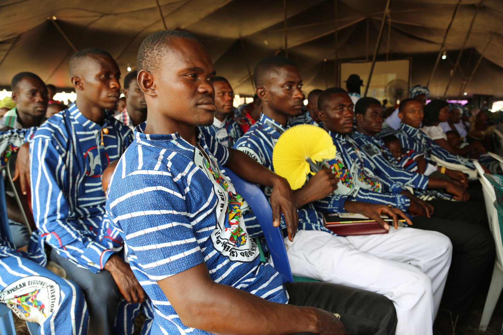 Group of men in blue and white striped clothing attending an event under a tent.