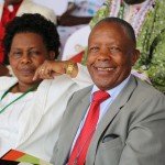 Smiling couple at an event, seated together, woman in white and man in a suit with a red tie.