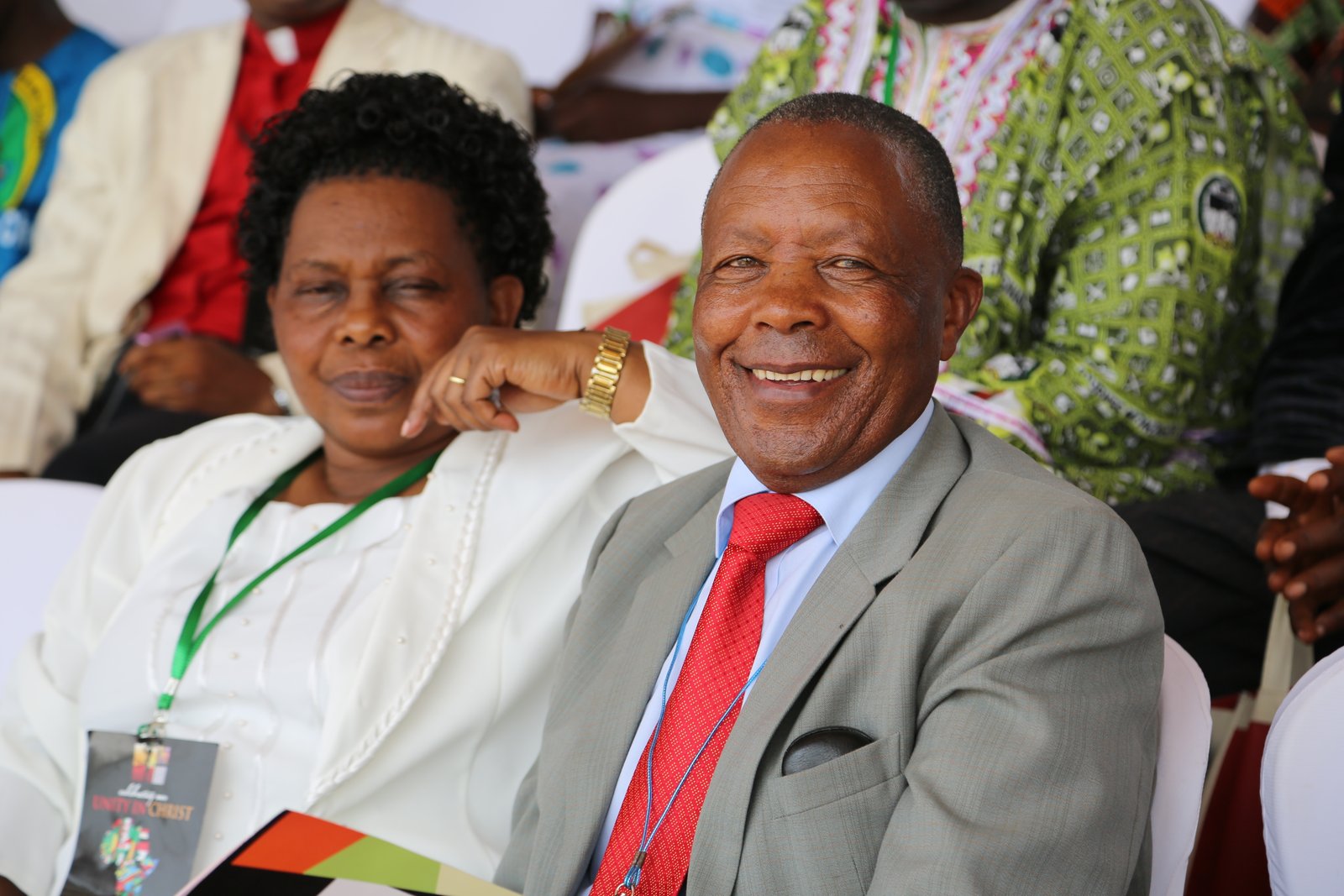 Smiling couple at an event, seated together, woman in white and man in a suit with a red tie.