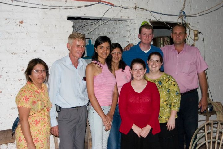 Group of people posing together indoors in casual attire, smiling, in front of a white brick wall.