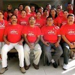 Group of people in matching red t-shirts smiling and posing for a team photo outdoors.