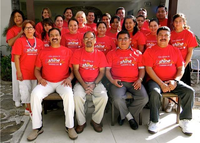 Group of people in matching red t-shirts smiling and posing for a team photo outdoors.