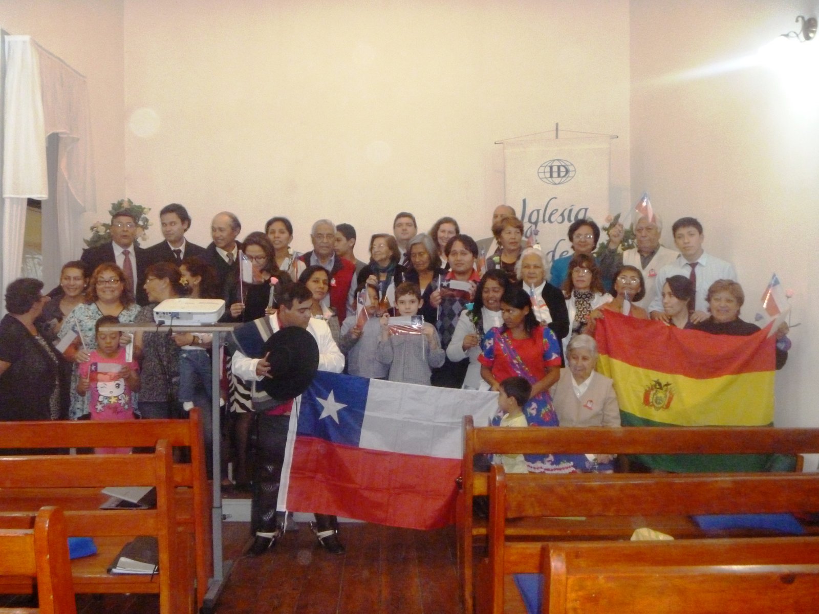Group at church event holding Chilean and Bolivian flags, celebrating multicultural gathering indoors.