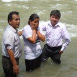 Three people standing in a river participating in an outdoor baptism ceremony.