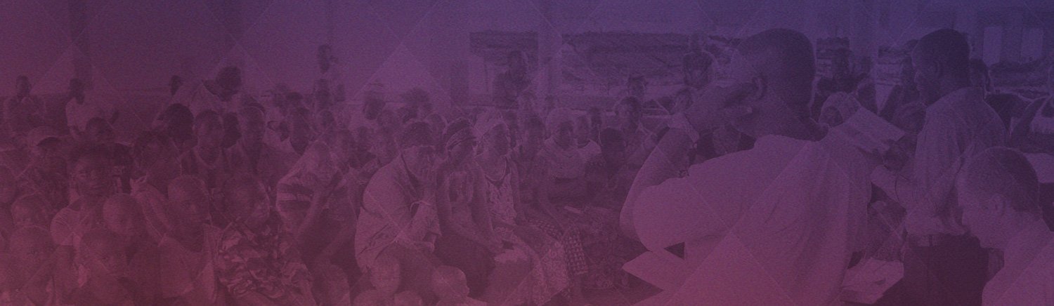 Community meeting with diverse attendees, all focused on a speaker inside a large hall.