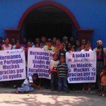 Group of people holding thank you banners in Spanish outside a blue building.