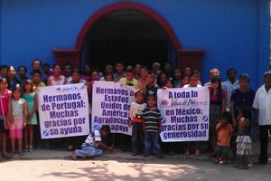 Group of people holding thank you banners in Spanish outside a blue building.