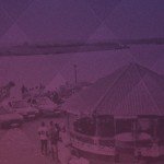 Scenic riverside with gathering, vehicles, and structures under a gradient filter, person observing the busy scene.