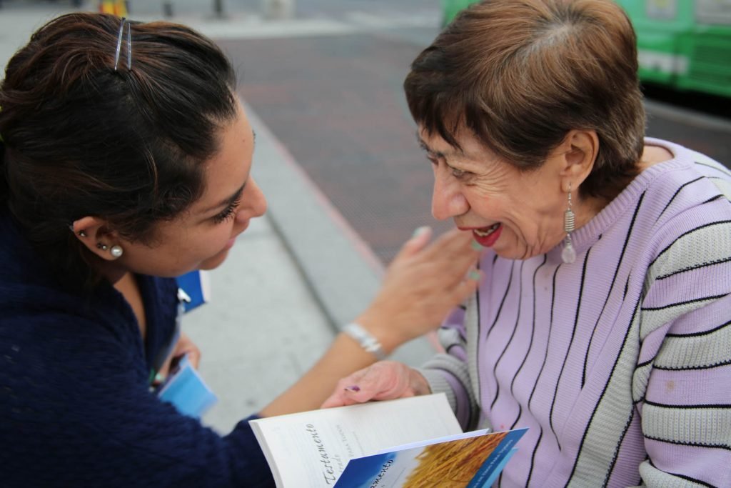 Two women share a joyful moment while reading a book together outdoors.