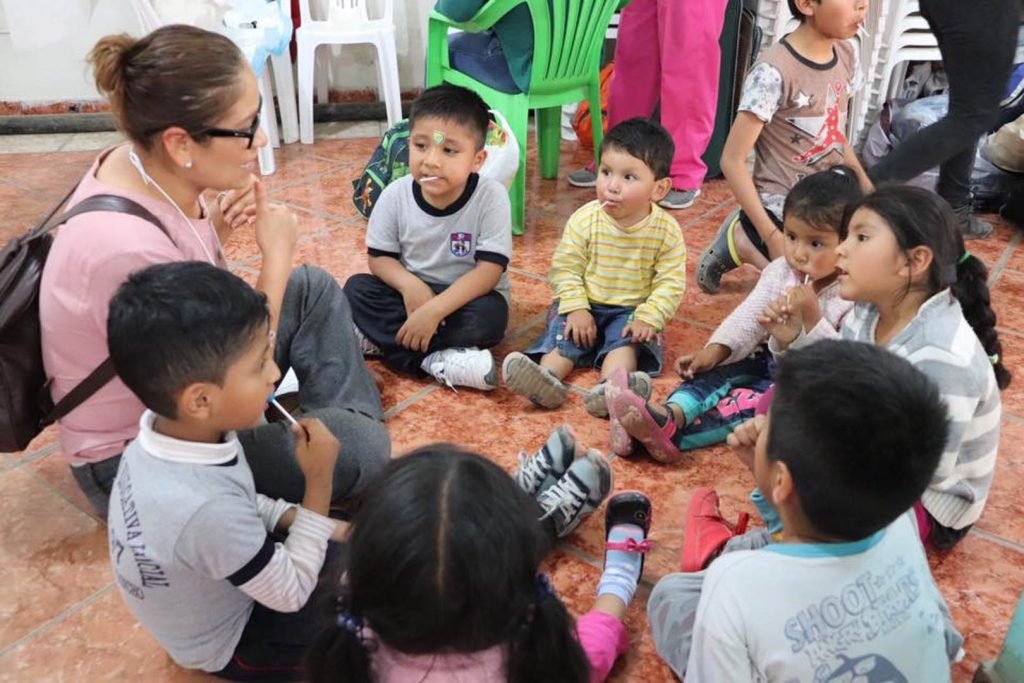 Teacher engaging with a group of children sitting on the floor, fostering learning and interaction in a classroom setting.