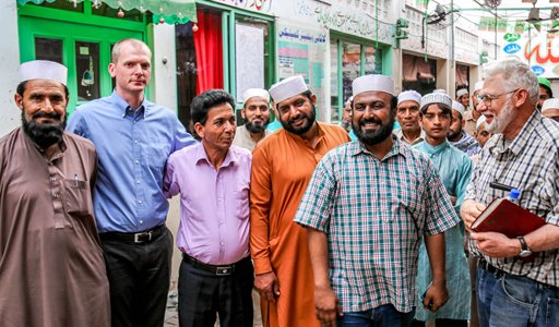 A diverse group of men stands together outdoors, smiling in a casual, social setting.